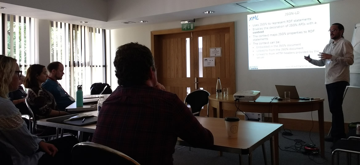 Linked Data Training - picture shows Kal Ahmed, the course leader, standing in front of a projection screen, explaining JSON-LD details to the learners sat in front of him.